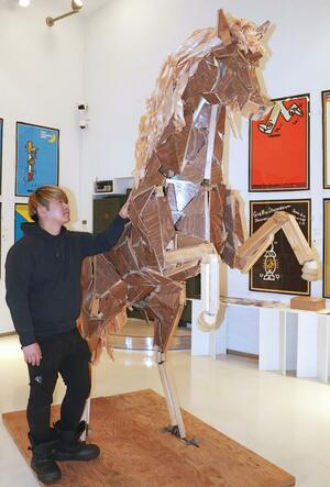 躍動感のある姿に仕立てた作品「午」を見上げる加治聖哉さん=21日、長岡市宮内2