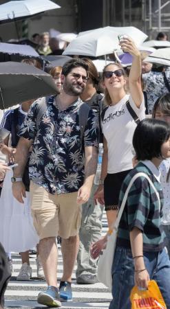東京・渋谷駅前のスクランブル交差点を撮影しながら渡る外国人=8月