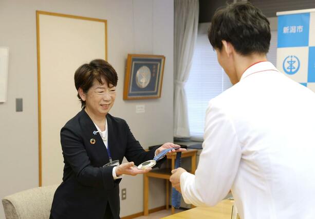古俣聖選手から銀メダルを受け取り、重さを確かめる野島晶子副市長(左)=9月30日、新潟市役所