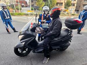 バイク利用者に交通事故への注意を促す警察官=18日午前、東京都江戸川区