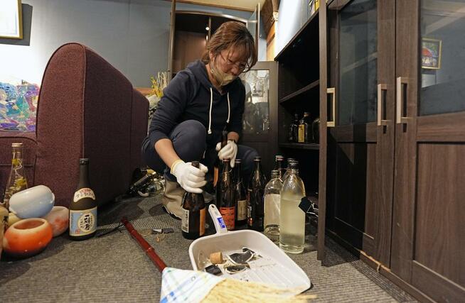 強い地震があった青森県八戸市で散乱した酒瓶を片付けるスナックの女性店主。「（瓶が）とび出さないように対策はしていたのに…」とため息をついた＝９日午後０時１３分