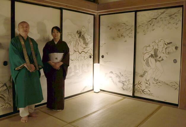 国上寺方丈講堂に描かれたイケメン絵巻第２弾。酒呑童子や役行者、義経と弁慶が描かれたふすまを背に立つ木村了子さんと住職の山田光哲さん＝１０日、燕市国上