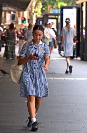 オーストラリア・シドニーで、スマートフォンを見ながら歩く女子生徒=5日(共同)
