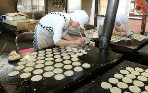 まめてんの生地を一枚一枚鉄板で焼く従業員=新潟市西蒲区小吉