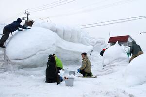 雪まつり開幕の前日、雨に見舞われる中、イルカやクジラの雪像づくりに取り組むひのスノーマンのメンバー=2月14日、十日町市下条3