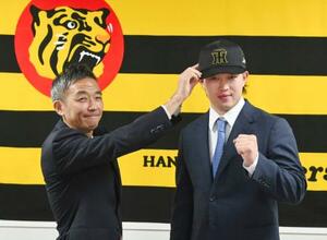 現役ドラフトでヤクルトから阪神に移籍し、帽子をかぶせてもらう浜田(右)=12日、兵庫県西宮市