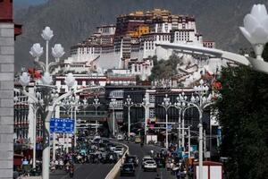 車や通行人でにぎわう中国チベット自治区ラサの大通り。奥はポタラ宮=6月(撮影・鷺澤伊織)