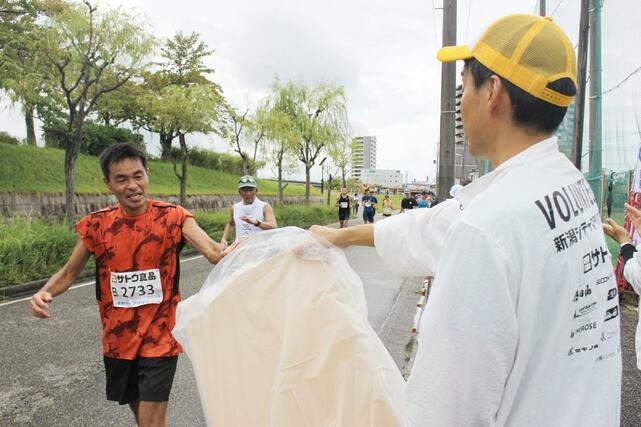 飲み終わった紙コップを捨てやすいようにごみ箱を持つボランティア＝12日、新潟市中央区