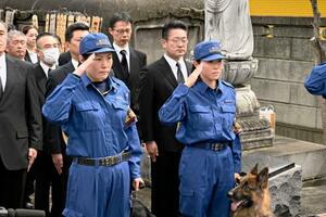 慰霊碑の前で敬礼する警察犬の担当者=23日午前、東京都板橋区