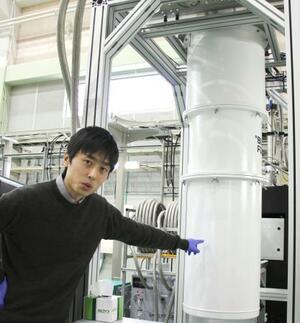 　量子コンピューターを示しながら、暗黒物質を検出する仕組みを説明する新田龍海さん＝２０２６年２月、茨城県つくば市の高エネルギー加速器研究機構