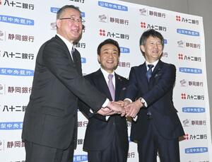 包括業務提携を結び、握手する(左から)八十二銀行の松下正樹頭取、静岡銀行の八木稔頭取、山梨中央銀行の古屋賀章頭取=27日午後、東京都千代田区