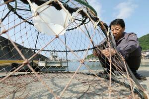 漁で使うカニ籠の編み目を直す本山誠さん。雌を逃がすため編み目の大きさが決められている=6月上旬、糸魚川市の能生漁港