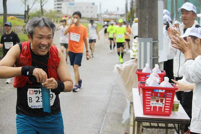 セルフ給水後、ボランティアの応援を受けて笑顔を見せるランナー＝12日、新潟市中央区