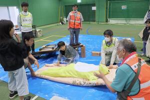 毛布を使ってけが人に見立てた人形の搬送を体験する親子=6月2日、新潟市西蒲区峰岡