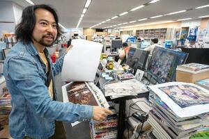 　「週刊ヤングジャンプ」編集部で校正刷りをチェックする大熊八甲。自席に椅子はなく、立って作業するスタイルだ＝２０２６年１月、東京・神保町の集英社