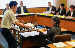 静岡県伊東市議会の百条委員会で証人尋問に応じ、確認のために東洋大の卒業アルバムを受け取る田久保真紀市長(右)=13日午前