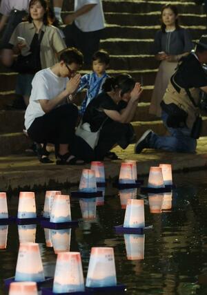 長岡空襲で多くの人が逃げ命を落とした柿川で、犠牲者を悼み平和を願う灯籠を流す人たち＝１日、長岡市旭町２