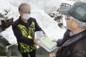雪が積もる中、利用者に弁当を届ける丸山富雄さん(左)=2月21日、魚沼市