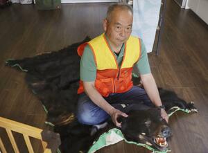過去に仕留めたクマの毛皮で作った敷物に座る舟山真人さん=14日、山形県小国町