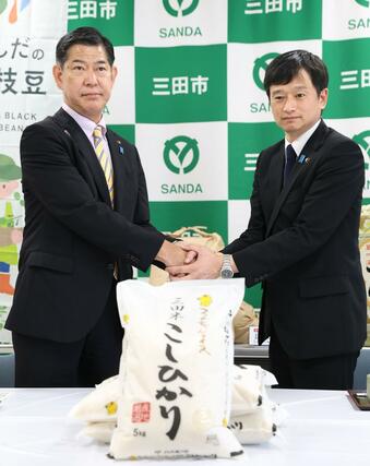 三田市産コシヒカリの試食後、三田市の田村克也市長（左）と握手を交わす上越市の中川幹太市長＝２９日、兵庫県三田市川除のＪＡ兵庫六甲三田支店