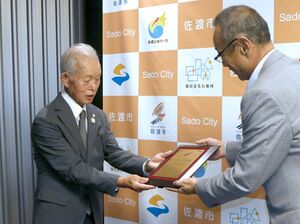 渡辺竜五佐渡市長から書状や記念品の盾を手渡された佐々木伸彦さん(左)=佐渡市役所