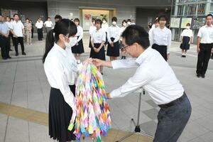 広島へ派遣される中学生を代表し、千羽鶴を受け取る中島穂乃花さん(手前左)=8月5日、上越市の上越妙高駅