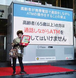 ATMの前で高齢者が携帯電話で通話するのを禁止した条例について、寸劇で説明する大阪府警の職員=1日午後、大阪市北区
