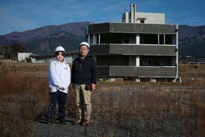 被災の爪痕が残る自社ビル前に立つ米沢多恵さん(左)と父の祐一さん。津波は地上約15メートルの屋上の煙突部分まで到達した。「多恵には教訓だけじゃなく、ここがすごくいい町だったことも伝えてほしい」=2025年12月、岩手県陸前高田市