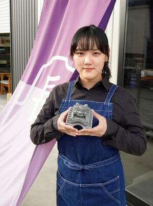 　瓦製小物の専門店で販売するミニ鬼瓦を持つ鬼瓦職人の長沢玲奈さん＝静岡市