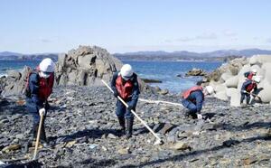 宮城県南三陸町の沿岸部で、行方不明者の手がかりを求め捜索する警察官=2024年3月
