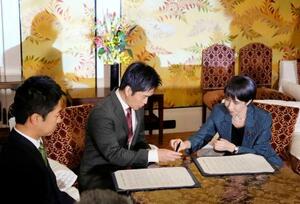 1本の万年筆で連立政権合意書に署名する自民党の高市総裁(右)と日本維新の会の吉村代表(中央)=20日午後、国会