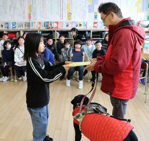 にいがた・盲導犬ハーネスの会会長の柾木裕明さん(右)に図書カードを渡す児童=新潟市中央区幸西4