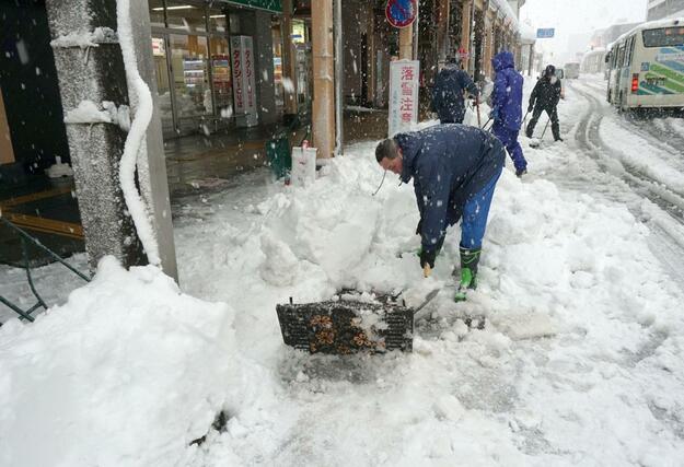 高田駅近くのアーケード街で、積もった雪を流雪溝に投げ入れる事業所の社員ら＝２４日、上越市仲町４