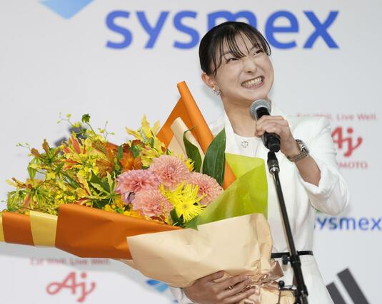 現役引退の記者会見で花束を手にマイクを握るフィギュアスケート女子の坂本花織＝１３日午前、神戸市内のホテル