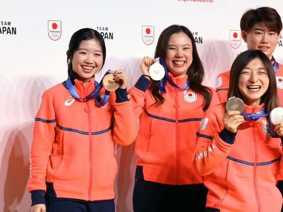 帰国後の記者会見でメダルを掲げてポーズをとる中井亜美選手（左）ら＝東京都内のホテル