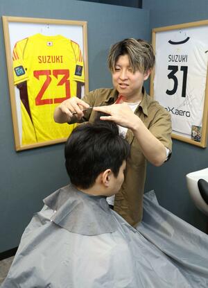 客の髪を切る斉田大輝さん。店には鈴木彩艶選手からプレゼントされたユニホームを飾っている＝２４日、新潟市中央区