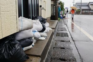 冠水した道路脇の民家では玄関前に土のうが積まれていた=15日、胎内市新栄町