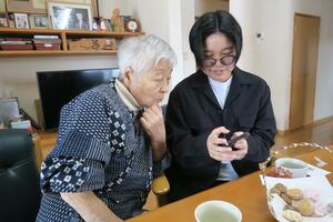 利用者にスマートフォンの使い方を教える学生(右)。スリーエスが橋渡し役となって、学生らの生活支援に取り組む=新発田市(スリーエス提供)