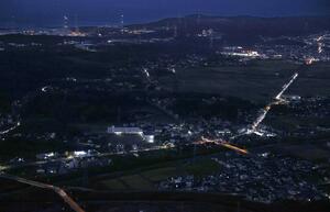 夜景に浮かび上がる東京電力柏崎刈羽原発(奥)と国道8号に連なる車列の明かり。国道8号は原発事故時の避難路として想定されている=柏崎市(本社ヘリから)