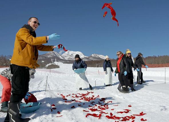 好天の中、トウガラシを雪に投げる外国人観光客ら=20日、妙高市