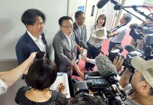 退陣の申し入れを決めた後、報道陣の取材に答える自民党県連の岩村良一幹事長(中央)=25日、県議会