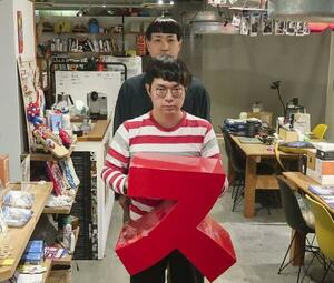 万博スイスパビリオンに置かれた「ス」いすを手にする花岡洋一さんと山根シボルさん