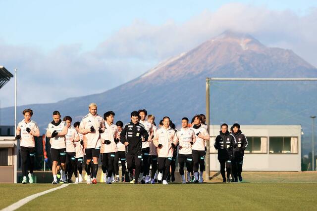 うっすらと冠雪した霧島連山をバックに体を動かす選手たち＝宮崎県都城市