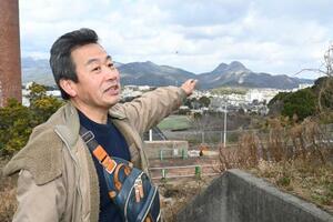 セメントの原料となる石灰岩の採掘で山頂が削られた香春岳を指し示す朴康秀さん。石炭を「黒ダイヤ」、石灰を「白ダイヤ」と呼ぶほど、鉱業は筑豊の産業の中心だった=2025年1月、福岡県田川市