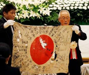 返還された日章旗を手にする菅田信博さん(右)と工藤公督さん=13日午前、北海道当麻町