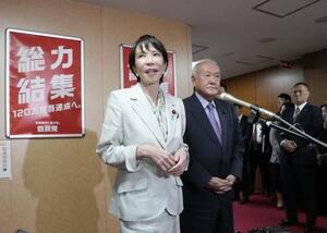 自民党本部で記者団の取材に応じる高市総裁。右は鈴木幹事長=7日、東京・永田町