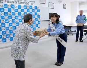 防犯機能付き電話機を手渡すTSUNEIさん(右)=上越警察署