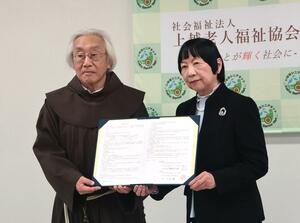 上越老人福祉協会の川室優理事長（右）とフランシスコ第三会マリア園の伊能哲大理事長が事業譲渡の契約書に署名した調印式＝上越市西城町２の高田西城病院