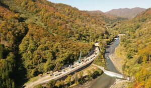 工事が進む福島県只見町の国道２８９号八十里越で色づく紅葉。奥が新潟県側、右は叶津川＝１０月３０日（小型無人機で撮影）