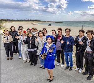 　青空の下、三線の弾き語りで沖縄の歌を披露するシャーバー千亜希。見守る大学生たちが手拍子を送った＝２０２６年３月、沖縄県豊見城市の豊崎美らＳＵＮビーチ